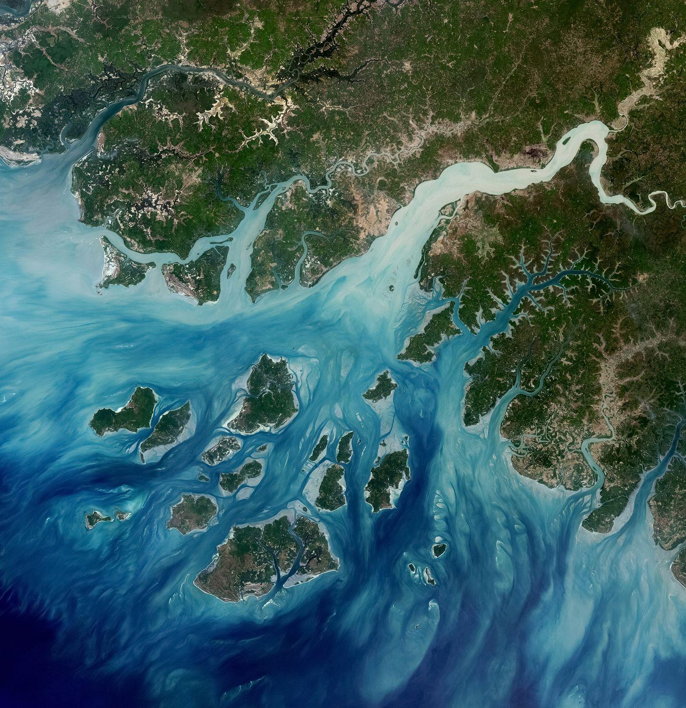Satellite view of a river delta meeting the sea, channels and low islands breaking the water into fragments