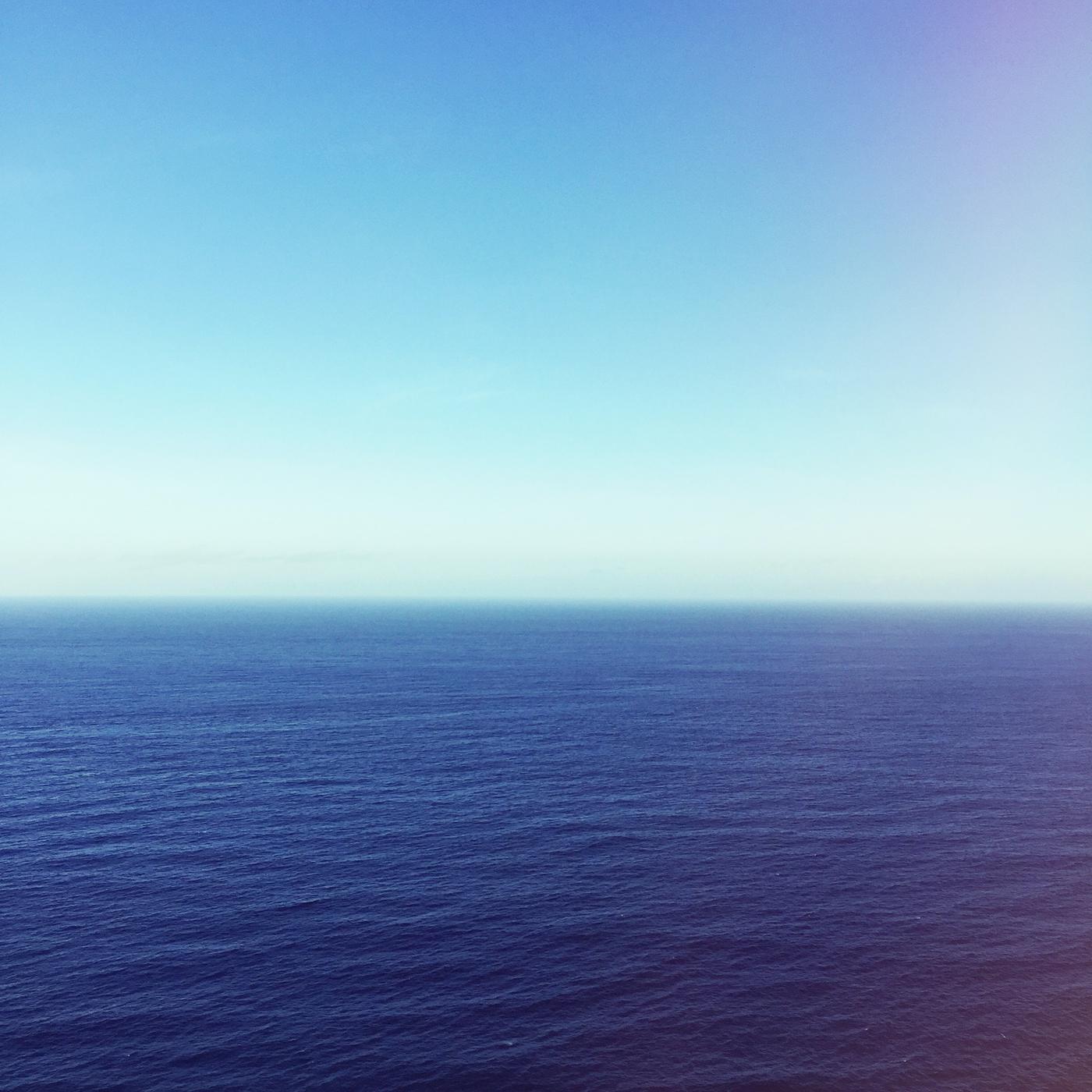 A pale hazy horizon where a flat sea meets a washed-out sky